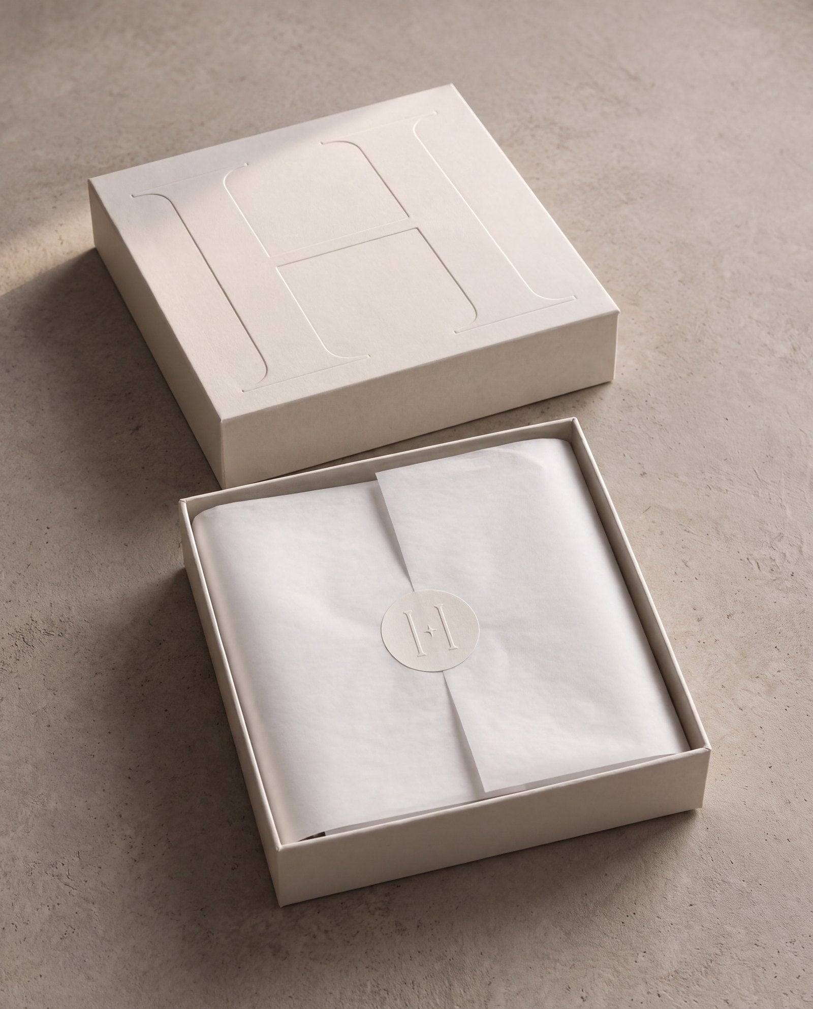 The Heir presentation box: the lid, embossed with a large H, beside the open box with the blanket wrapped in tissue and sealed with the monogram